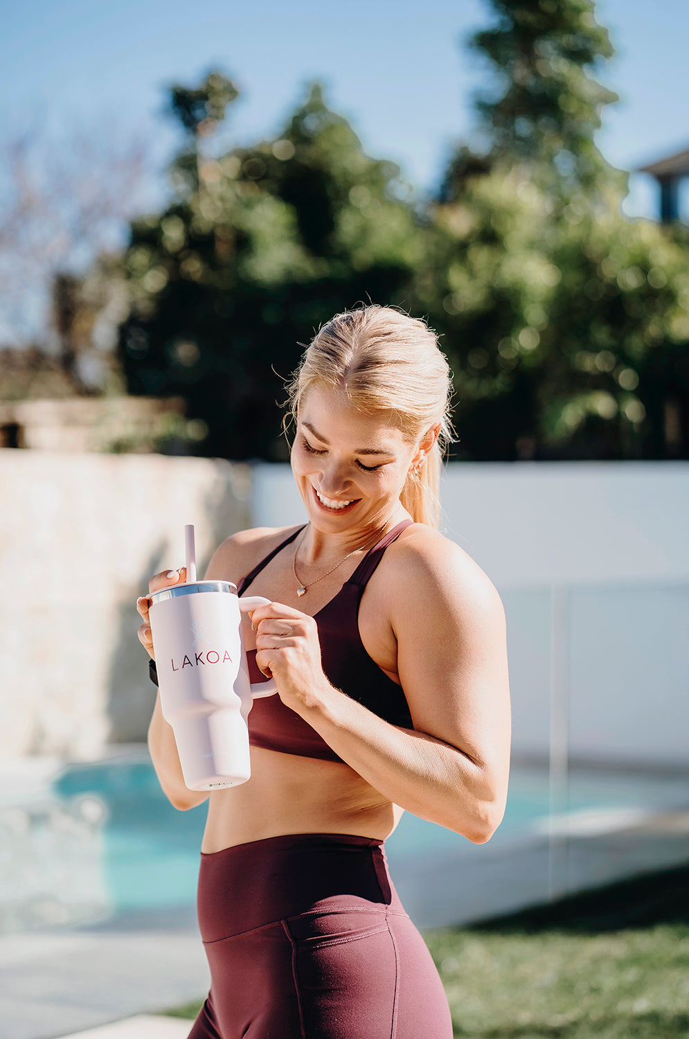 Woman holding a LAKOA tumbler by a pool with greenery in the background